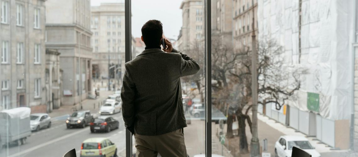 Professionnel expatrié regardant par la fenêtre de son bureau pendant un appel, contexte habituel du burnout dans la population expatriée à Madrid